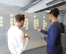 Two individuals collaborating and organizing sticky notes on a glass wall for brainstorming or planning purposes.