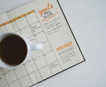 A top-down view of a white cup of coffee placed on an open planner with a monthly calendar layout for November.