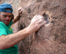 Man wearing a hat and green shirt doing rock climbing.
