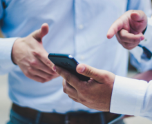 Two men exchanging details with one showing to the other using his mobile phone.