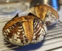 Two golden-brown artisanal bread loaves rest on a wire rack, their crusts scored and dusted with flour.