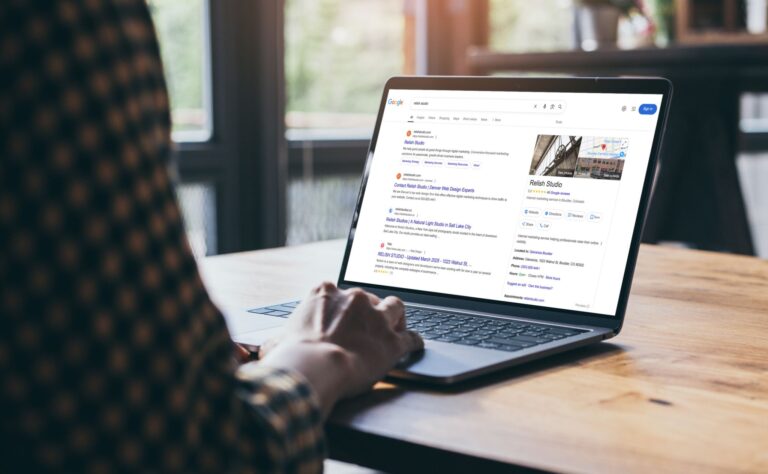 A person using a laptop at a wooden table searches for “Relish Studio” on Google.