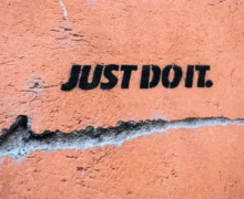 The phrase “JUST DO IT.” is spray-painted in bold black stencil lettering on a weathered orange wall.
