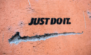 The phrase “JUST DO IT.” is spray-painted in bold black stencil lettering on a weathered orange wall.