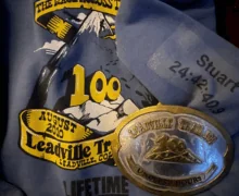 A Leadville Trail 100 race shirt and finisher’s buckle engraved “Under 25 Hours,” with the name “Stuart” and time “24:42:09” printed on the sleeve.