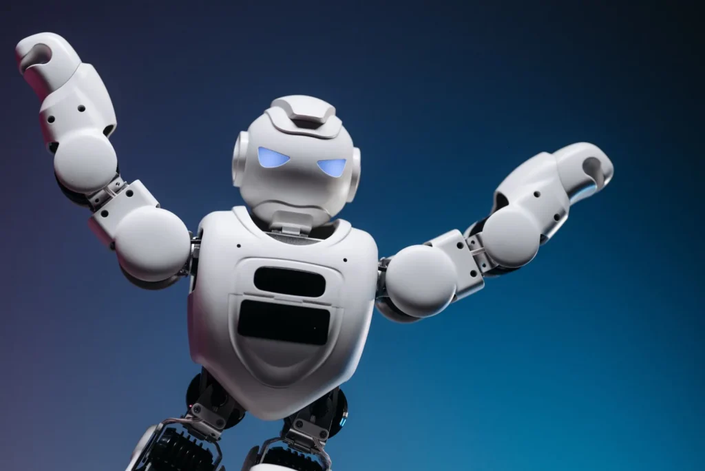 White humanoid robot with glowing blue eyes raising both arms in celebration against a dark blue background